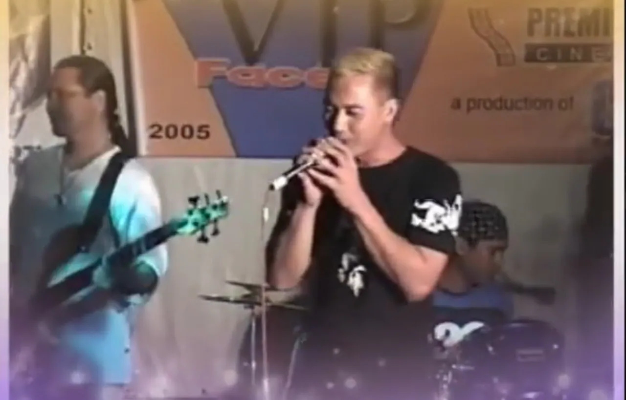 Archival live performance with a singer at a microphone and a 2005 backdrop.